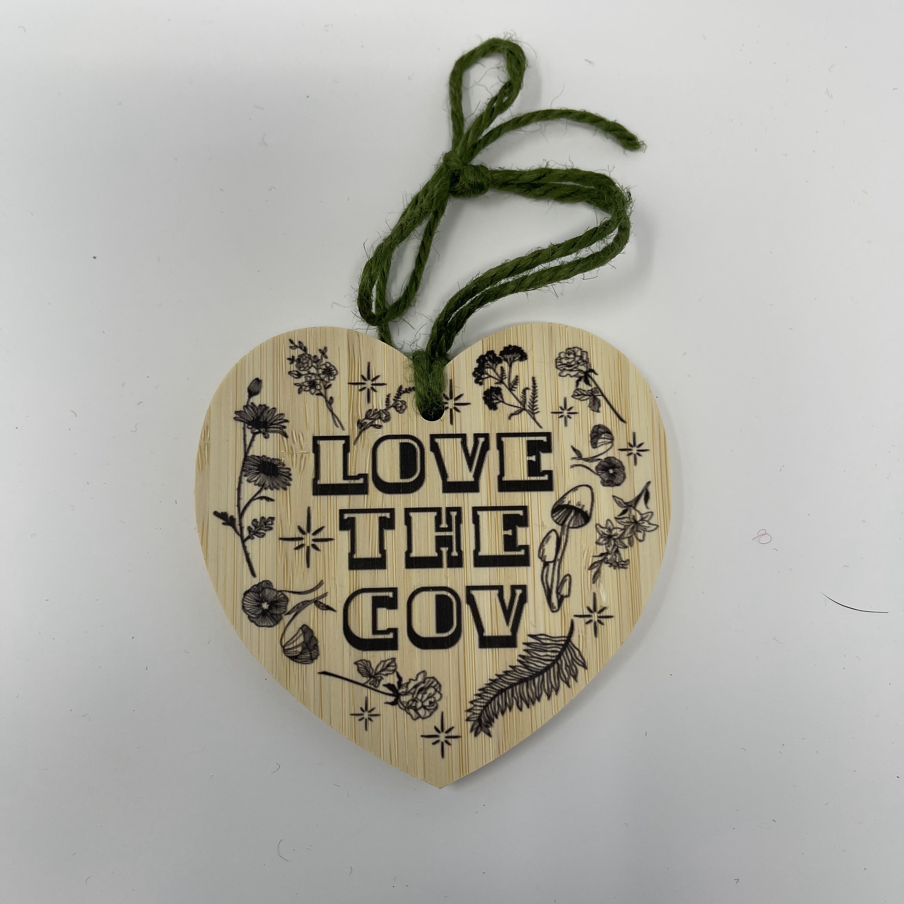 #62 Wood heart with "LOVE THE COV" in black text and flora design. Hung on green yarn. 3.5x3.5x0.25"