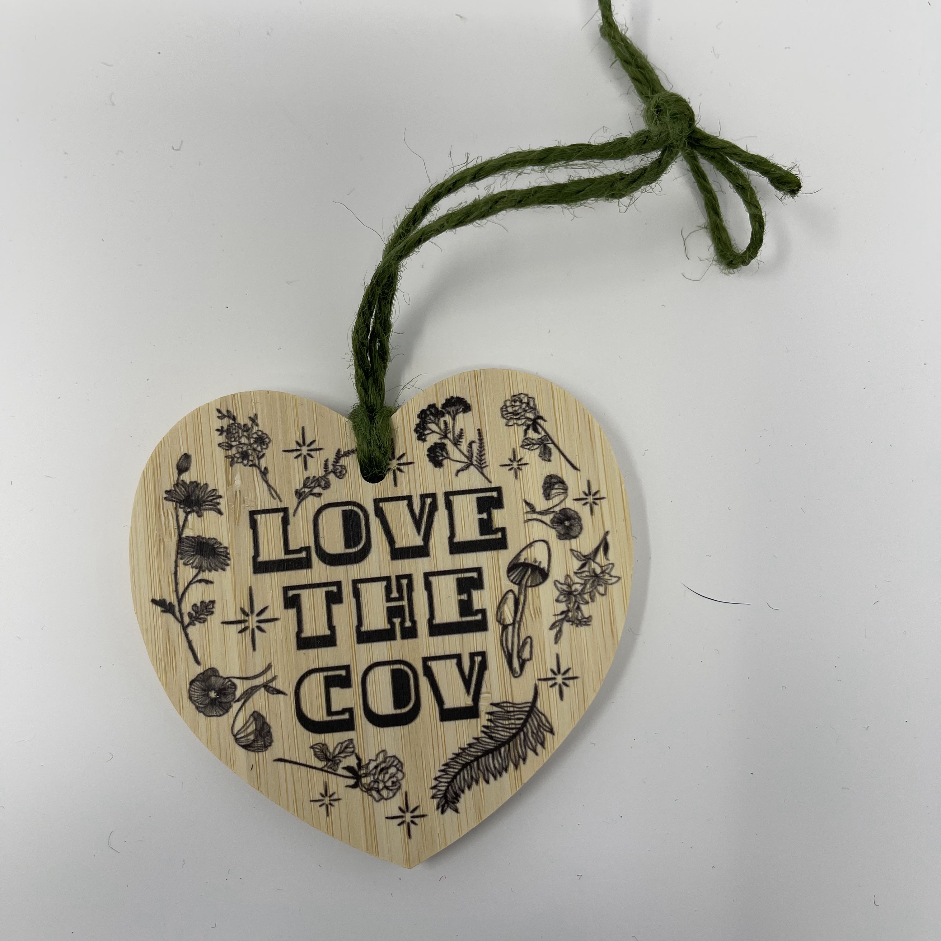 #7 Wood heart with "LOVE THE COV" in black text and flora design. Hung on green yarn. 3.5x3.5x0.25"